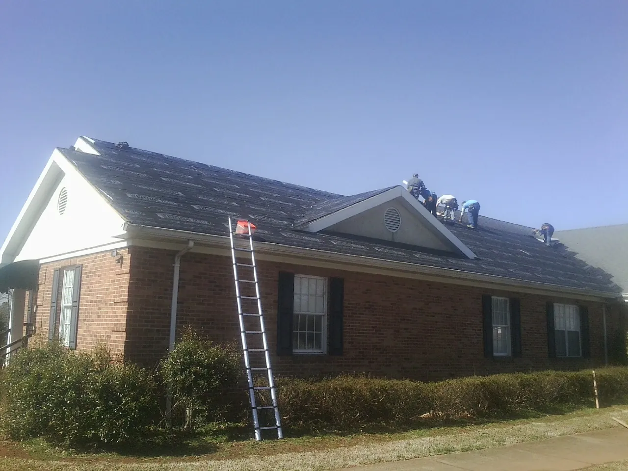 Crew tearing shingles off a brick ranch roof with a ladder set — Metal Roof Repair work by our crew in Ivoryton