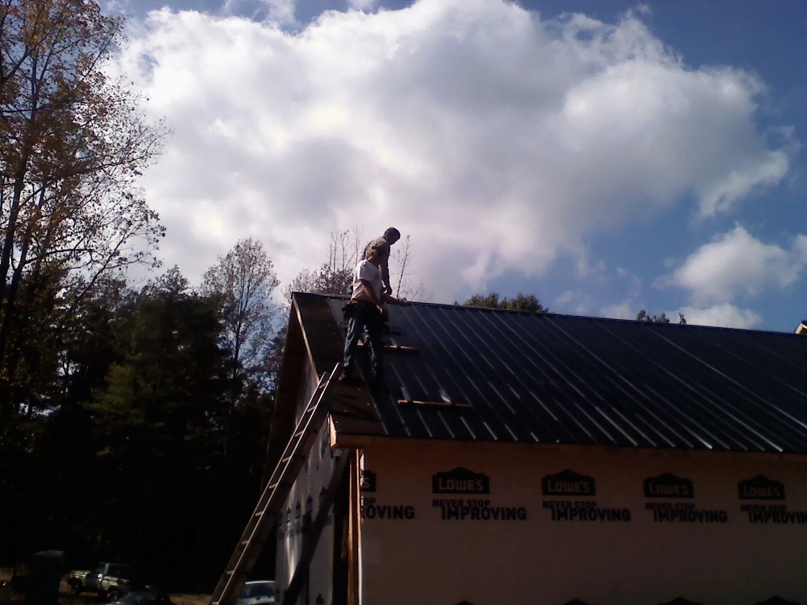 Roofer fastening dark metal panels high against a cloudy sky, from a Roof Inspection job in Ivoryton