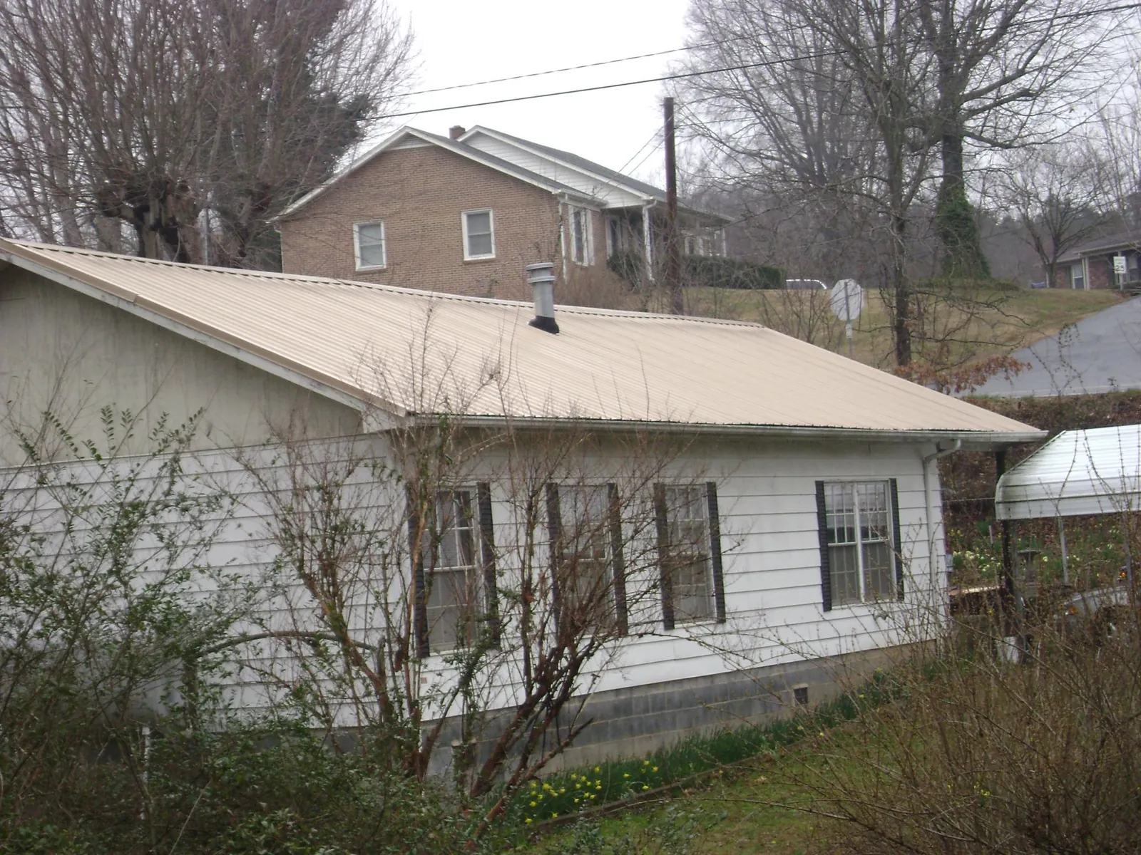 Tan metal roof on a white sided house set into a hillside — Commercial Roofing by Roofing Brothers in Ivoryton